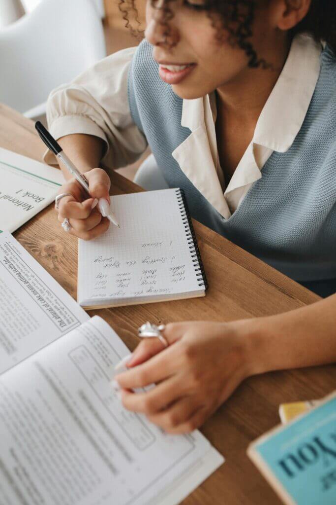 Focused young woman taking notes from textbooks, embodying active learning and education.