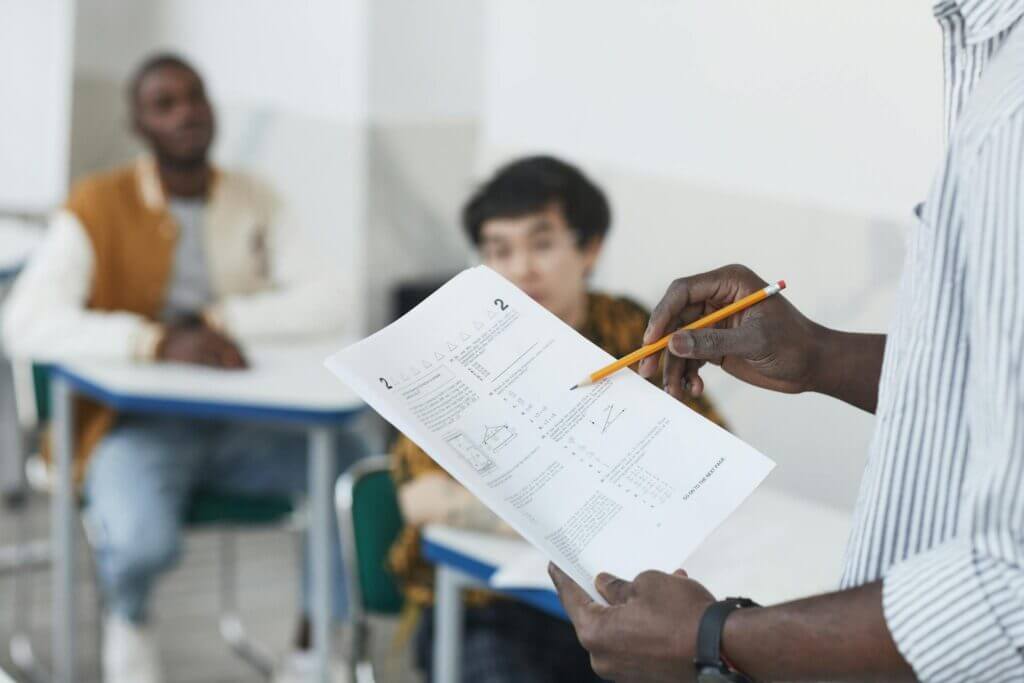 Students working on an exam with a teacher overseeing in a classroom.